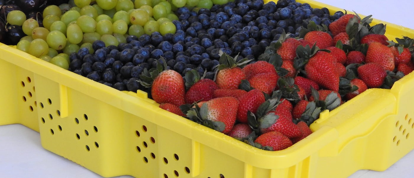A yellow perforated berry tray filled with cherries, grapes, blueberries and strawberries